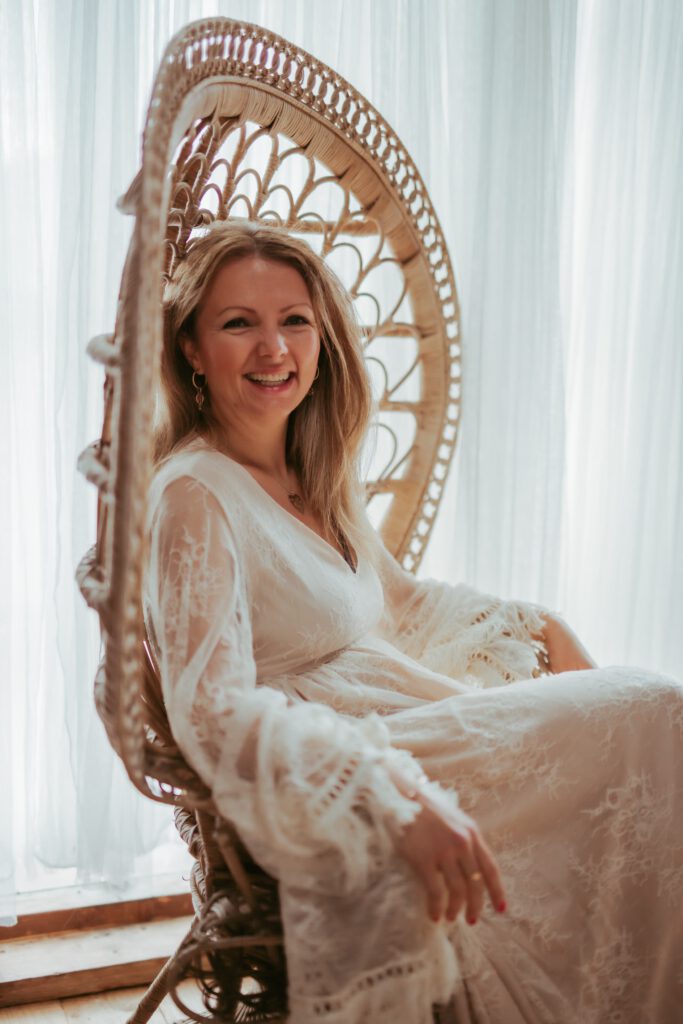 Julija sitter i vacker stol, vit klänning. Sorgbearbetning och NLP Coaching för kvinnor med Julija Kondovska